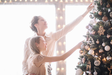 mom and her little daughter decorating the Christmas tree