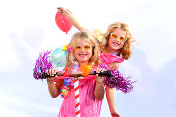 Twin sisters play together riding an imaginative bicycle. They use a rusty handlebar they found in the garage. They fit it with fringes, a windmill and an orange plastic horn.