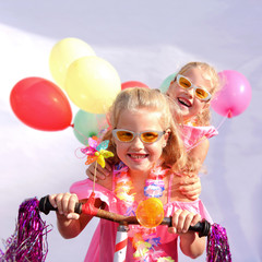 Twin sisters play together riding an imaginative bicycle. They use a rusty handlebar they found in the garage. They fit it with fringes, a windmill and an orange plastic horn.