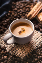 
    Cup of coffee in the middle of coffee beans with biscuits and tablecloth. Grained product. Hot drink. Close up. Harvesting. Natural background. Energy. Fresh espresso with beans on the foam.