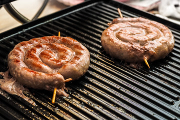 Fried spiral sausages on an electric barbecue BBQ grill. Homemade menu.