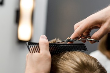 Barber cuts the little blond boy with scissors and combs in the hair salon close-up