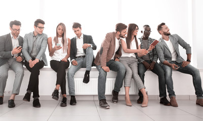 group of young people using their gadgets sitting in the lobby of the office