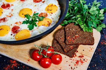 Fried eggs in a frying pan with cherry tomatoes and bread for breakfast on a black background.