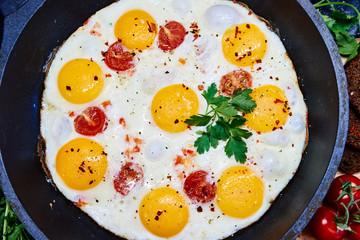 Fried eggs in a frying pan with cherry tomatoes and bread for breakfast on a black background.