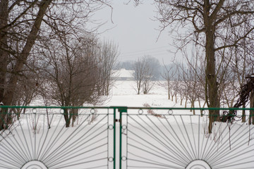 Winter landscape. Metal fence gate in the foreground, and in the background arable fields covered with white snow.