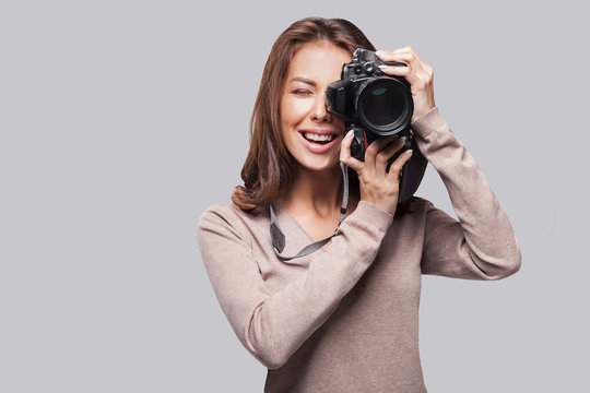Woman photographer is taking images with dslr camera. Isolated studio shot