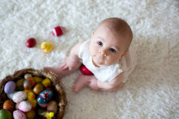 Cute little toddler baby boy, playing with colorful easter eggs and little decorative ducks,...