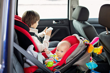 Little baby boy and his older brother, traveling in car seats, going on a holiday