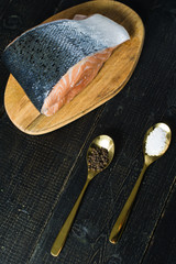 salmon on a wooden chopping Board, spoon with salt and pepper on black background, side view