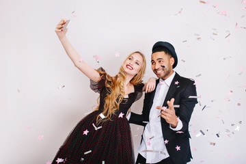 Amazing cute couple in love celebrating great party in tinsels, making selfie on white background....
