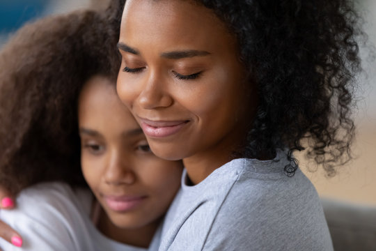 Close up of young black mother hugging teenage daughter, fell love and affection, caring African American mom hold teen girl in arms, embracing, having intimate moment together as best friends