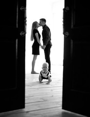 Baby boy crawls at the floor on background of his kissing parents.