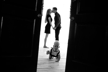 Baby boy crawls at the floor on background of his kissing parents.