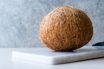 Fresh Organic Brown Raw Coconut on White Marble Board.