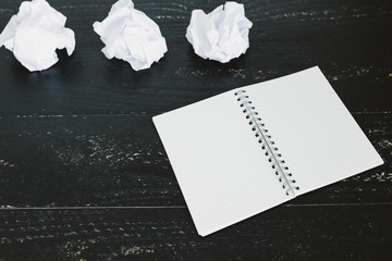 set of scrunched paper balls and empty notepad on dark moody background