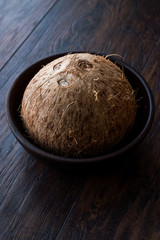Fresh Organic Brown Raw Coconut in Dark Wooden Bowl.