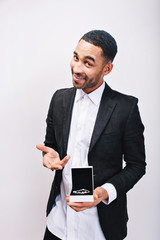 Handsome man in white shirt and elegant black jacket holding jewelry gift in hands and smiling to camera on white background. Holidays, present, cheerful mood, ornamentation, true positive emotions