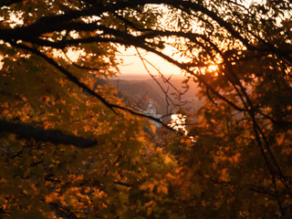 Monastery photographed through yellow foliage of autumn forest. Sunset in monastery, Ukraine. Autumn nature landscape. Yellow leaves on tree branch. Blurred background. Selective soft focus