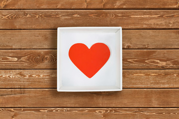 Red paper heart in white cardboard box on wooden wall background. Flat lay. Top view. Valentine's Day concept