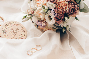 gold rings are next to a wedding bouquet and a wooden box with an engraving