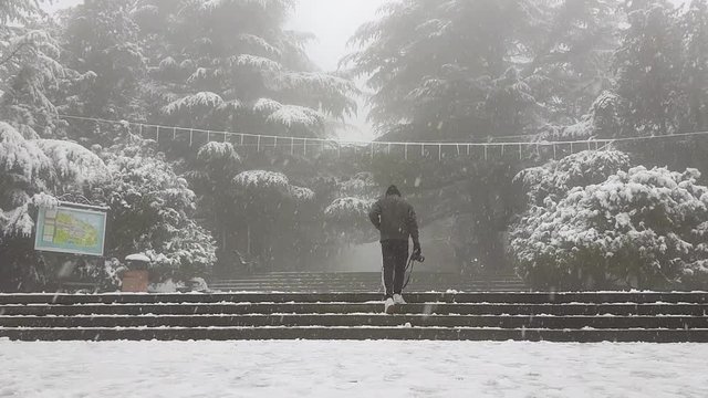 Teenager photographer wearing black adidas jogger pants while walking during a snowfall in the Mtatsminda park in Georgia