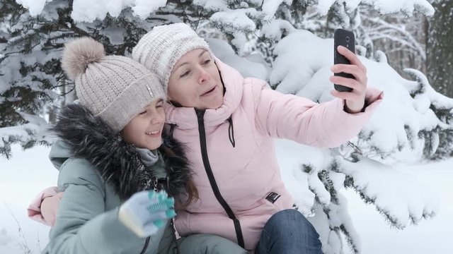 Happy family is photographed on the phone. Mother and child take pictures on a smartphone in the winter park.