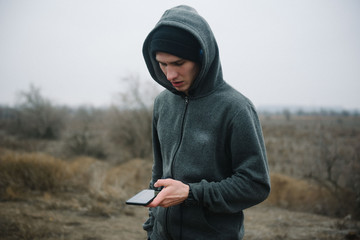 A man stands on the road with headphones looking for a track in the phone