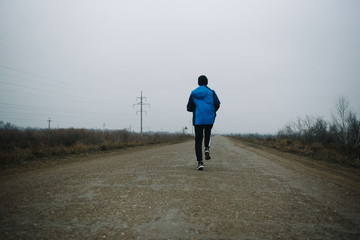 A man runs in headphones on the road. Stroke in pants and sneakers