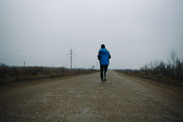 Obraz premium A man runs in headphones on the road. Stroke in pants and sneakers