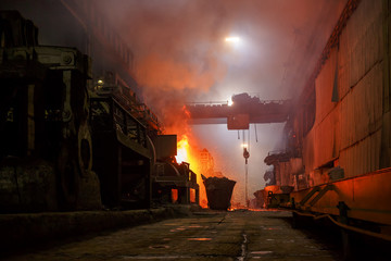 Copper production at the metallurgical plant. Large industrial structures, ore buckets, cranes and bright flame. Indoors a lot of fumes as a result of smelting metal.