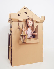 Little princess in crown play with her cardboard castle. True emotion of happiness of the child.