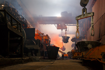 Copper production at the metallurgical plant. Large industrial structures, ore buckets, cranes and workers. Indoors a lot of fumes as a result of smelting metal.