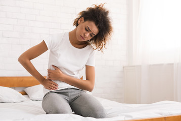 African-american girl suffering from abdominal pain on bed