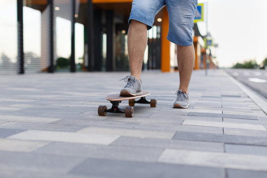 Close up street picture of men skateboarding in city with one foot placed on board and pushing off with the other/ man riding longboard, selective focus on boy's foot/ lifestyle and sport concept.