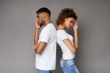 Upset couple standing back to back on gray background