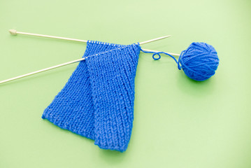 Bright knitted  scarf with knitting needles. On green background. Minimalism top view contrast. Horizontal vie several objects