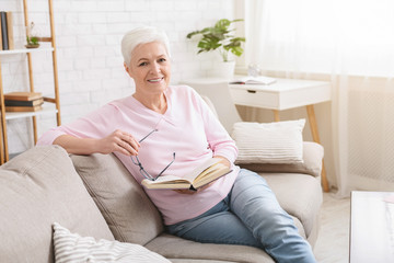 Senior woman resting on sofa and reading book