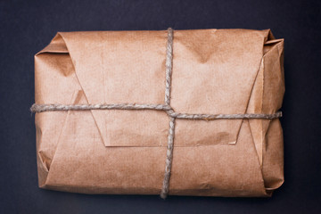 Craft wrapped package on black background. Parcel with hemp cord. 