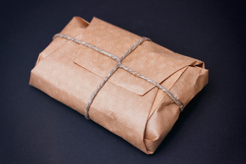 Craft wrapped package on black background. Parcel with hemp cord. 