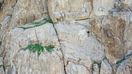 A man climbs up the cliff. Active leisure and sports. Climb up the rock. Shooting from the air. Aerial photography. Extreme, active rest, freedom. Beautiful nature, rock, wall, greenery.
