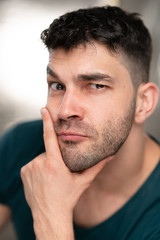 Fototapeta premium Handsome caucasian white male with black short hair and stubble with blue t shirt pondering