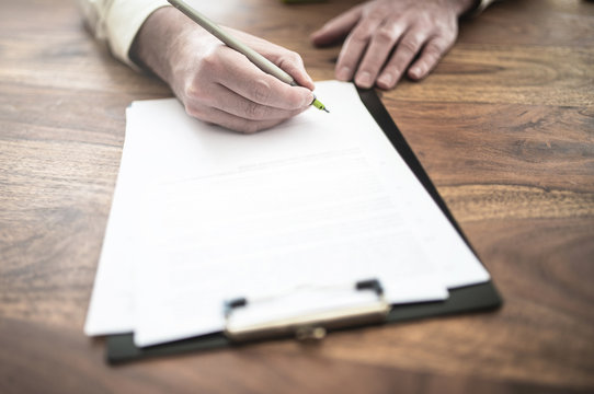 close-up of man signing contract at wooden desk