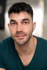 Fototapeta premium Handsome caucasian white male with black short hair and stubble with blue t shirt with a smirk