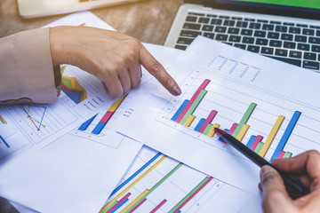 Two business women review and analyzing income charts and graphs with modern laptop computer. Close up businesswomen finger pointing to graph. Business analysis and strategy concept.