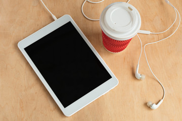 Tablet with blank black screen with earphones and a cup of coffee top view. Office morning concept. Wireless technology.