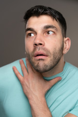 Fototapeta premium Handsome caucasian white male with black short hair and stubble with light blue t shirt looking embarassed