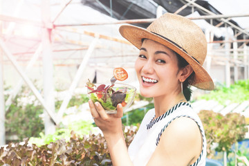 Young Asian woman eating veggie salad with hydroponics farm in background