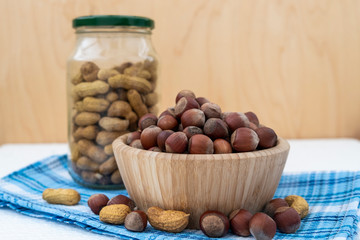 Hazelnuts and peanuts in the composition. Wooden bowl and glass jar