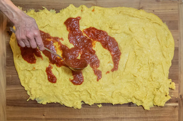 Cooking polenta, typical, traditional, Italian food made with cornmeal and water. Top view of wooden pastry with yellow polenta. A woman pours the sauce. Lunch with the family.